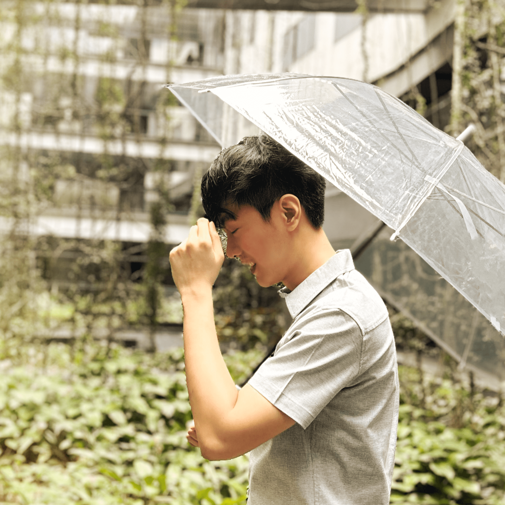 Boy holds clear umbrella standing in a bright, sunny space.